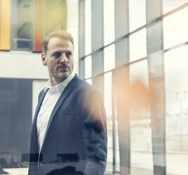 Confident businessman looking out of window - UUF13318