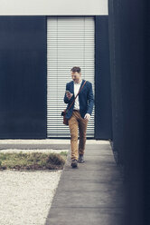 Geschäftsmann, der im Freien spazieren geht und auf sein Smartphone schaut - UUF13320