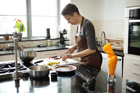 Frau schneidet Bananen für die Zubereitung einer Torte, lizenzfreies Stockfoto