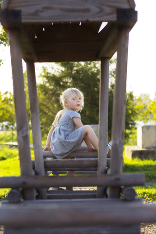 Porträt eines Mädchens, das auf einer Holzkonstruktion im Park sitzt, lizenzfreies Stockfoto