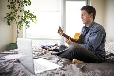 Man using laptop computer for learning guitar at home - CAVF35899