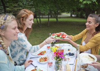 Friends having food at breakfast table in backyard - CAVF36010