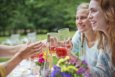 Happy friends toasting drinks while sitting at breakfast table in backyard - CAVF36011