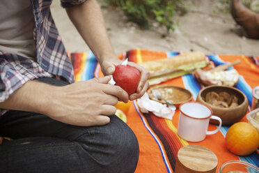 Nahaufnahme eines Mannes, der auf einem Feld sitzend Obst schneidet - CAVF36049