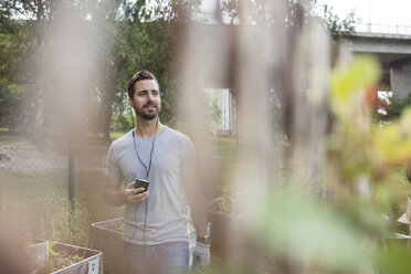 Mittelgroßer erwachsener Mann benutzt Mobiltelefon im Gemeinschaftsgarten - MASF02258