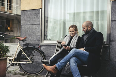 Mid adult business people using smart phone on bench against building - MASF02263