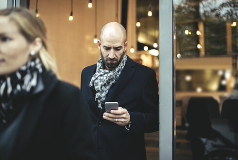 Mittlerer erwachsener Geschäftsmann, der beim Verlassen eines Cafés ein Mobiltelefon benutzt - MASF02264
