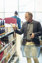 Älterer Mann liest Etikett auf Lebensmittelverpackung im Supermarkt - MASF02277