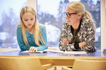 Mittlerer erwachsener Lehrer mit Mädchen, das am Schreibtisch im Klassenzimmer ein Buch liest - MASF02281