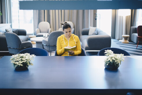 Mid adult businesswoman reading book in office lobby - MASF02288
