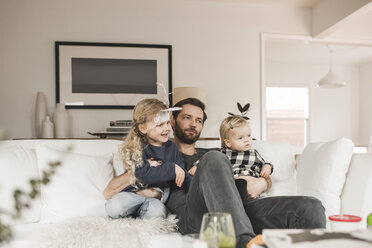 Mittlerer erwachsener Mann mit Töchtern, die zu Hause auf dem Sofa im Wohnzimmer sitzen - MASF02296