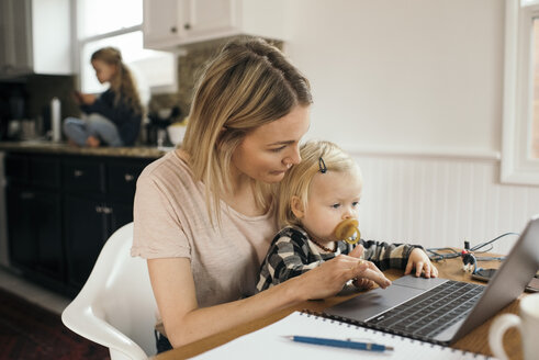 Mid adult woman using laptop while daughter sitting on her lap at home - MASF02301