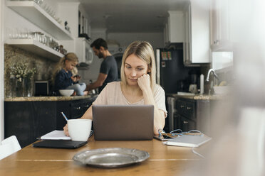 Mittlere erwachsene Frau benutzt Laptop am Tisch mit Familie in der Küche zu Hause - MASF02302