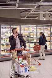 Älterer Mann, der mit seinem Handy telefoniert, während eine Frau auf eine Kühlvitrine im Supermarkt schaut - MASF02303