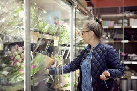 Ältere Frau kauft Blumen aus einer Vitrine im Supermarkt, lizenzfreies Stockfoto