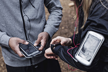 Mittelteil von Sportlern, die eine Smartwatch und ein Mobiltelefon im Wald benutzen - MASF02310