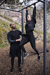 Mid adult man assisting woman exercising on monkey bars in forest - MASF02311