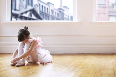 Mädchen mit Ballettschuhen, das auf einem Hartholzboden im Studio sitzt - CAVF36138