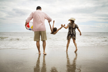 Rear view of playful parents picking daughter at beach - CAVF36162