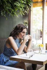 Young woman drinking coffee at table in restaurant - CAVF36201