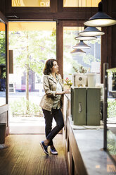 Thoughtful woman standing at checkout counter in cafe - CAVF36210