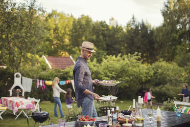 Mann trägt Teller am Esstisch im Hinterhof während einer Gartenparty - MASF02312