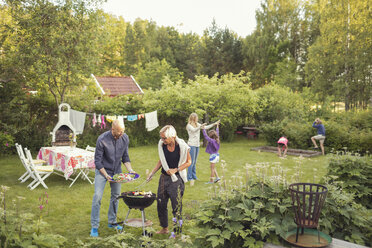 Mann und Frau kochen Gemüse auf dem Grill mit Kindern, die eine Gartenparty genießen - MASF02313