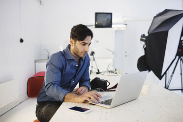 Male blogger using laptop at desk in creative office - MASF02328