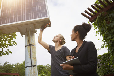 Gartenarchitekt mit niedrigem Blickwinkel, der das Solarmodul durch einen Kollegen mit Tablet-Computer einstellt - MASF02330