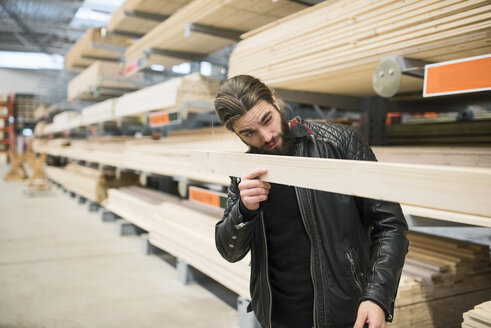 Männlicher Kunde begutachtet ein Holzbrett in einem Baumarkt - MASF02334