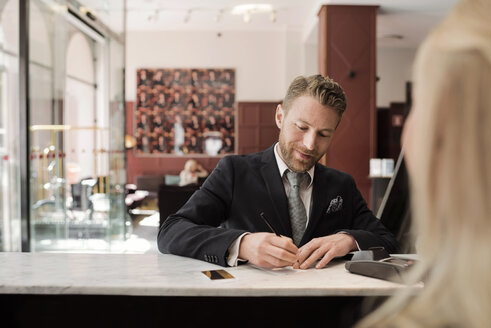 Reifer Geschäftsmann, der an der Hotelrezeption mit Kreditkarte bezahlt - MASF02346