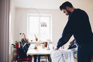 Man ironing while woman sitting on chair by dining table at home - MASF02358