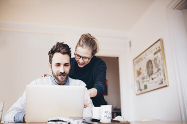 Low angle view of happy couple looking at laptop in domestic room - MASF02359