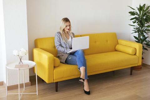 Businesswoman sitting on yellow couch, using laptop stock photo