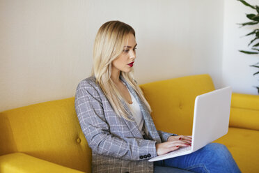 Geschäftsfrau sitzt auf einer gelben Couch und benutzt einen Laptop - EBSF02341