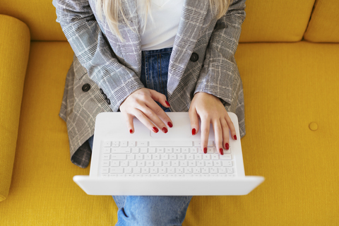 Geschäftsfrau sitzt auf einer gelben Couch und benutzt einen Laptop, lizenzfreies Stockfoto