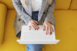 Businesswoman sitting on yellow couch, using laptop - EBSF02342