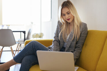 Geschäftsfrau sitzt auf einer gelben Couch und benutzt einen Laptop - EBSF02345