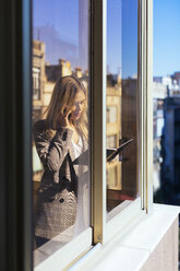 Young businesswoman standing at the window, talking on the phone - EBSF02350