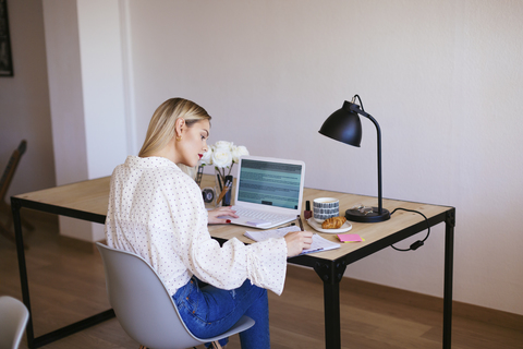 Blonde Geschäftsfrau sitzt am Schreibtisch und arbeitet, lizenzfreies Stockfoto
