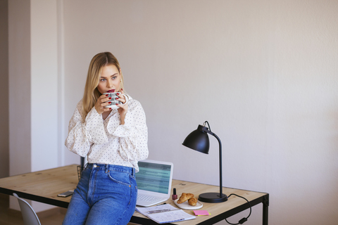 Junge Frau arbeitet im Büro, macht eine Pause, trinkt Kaffee, lizenzfreies Stockfoto