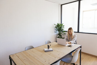 Blonder Büroangestellter sitzt am Schreibtisch und benutzt einen Laptop - EBSF02377