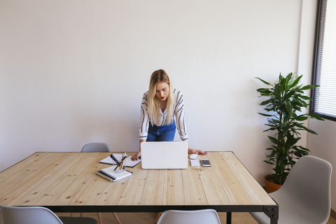 Young businesswoman standing at desk, using laptop stock photo