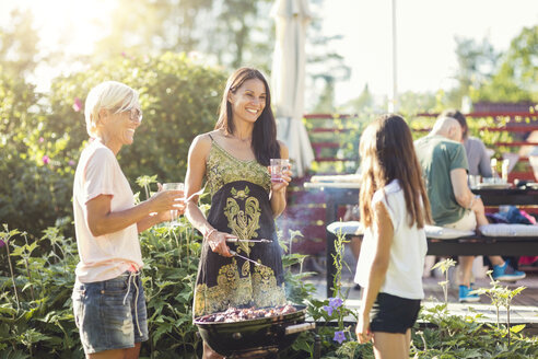 Glückliche Frauen bereiten Essen auf dem Grill vor, während sie ein Mädchen im Hinterhof betrachten - MASF02377