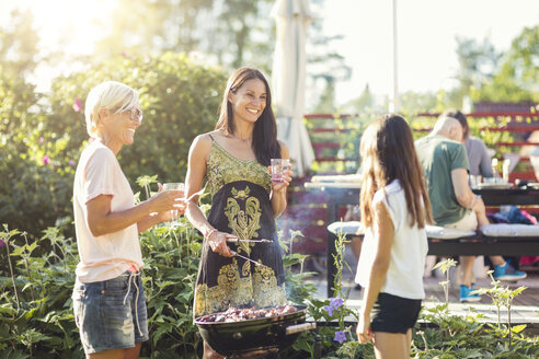 Happy women preparing food on barbecue while looking at girl in back yard - MASF02377