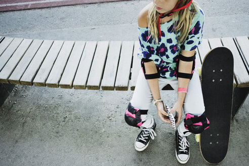Hohe Winkel Ansicht von Mädchen mit Skateboard hält Handy beim Sitzen auf der Bank im Park - MASF02380