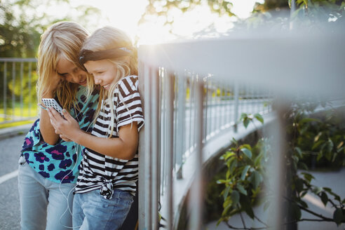 Glückliche Freunde benutzen ihr Handy und lehnen sich an ein Geländer - MASF02383