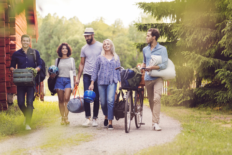 Happy friends with bicycle and luggage walking on pathway by cottage stock photo