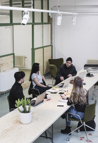 Hochformatige Ansicht von vier Unternehmern, die am Schreibtisch in einem kreativen Büro diskutieren, lizenzfreies Stockfoto