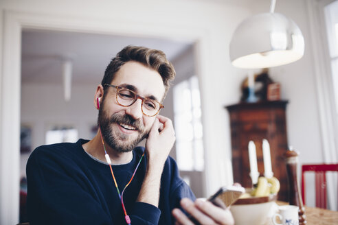 Glücklicher Mann, der zu Hause mit seinem Mobiltelefon Musik hört - MASF02414